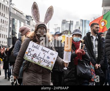 19 February 2022, Hessen, Frankfurt/Main: A woman carries an Easter bunny mask, a cardboard syringe and a placard reading 'Soon the booster bunny will be here' during a demonstration of several thousand people against Corona measures and compulsory vaccination in downtown Frankfurt. Photo: Frank Rumpenhorst/dpa Stock Photo