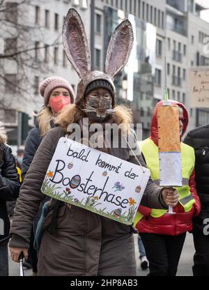 19 February 2022, Hessen, Frankfurt/Main: A woman carries an Easter bunny mask, a cardboard syringe and a placard reading 'Soon the booster bunny will be here' during a demonstration of several thousand people against Corona measures and compulsory vaccination in downtown Frankfurt. Photo: Frank Rumpenhorst/dpa Stock Photo
