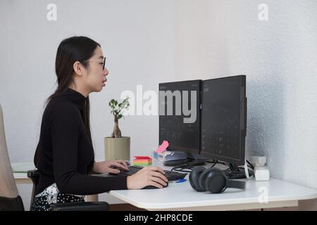 Young asian trader analyst using the computer to analyze cryptocurrency graphs. Stock Photo