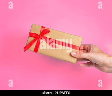 Gift box craft paper with red bow in hand on pink background Stock Photo