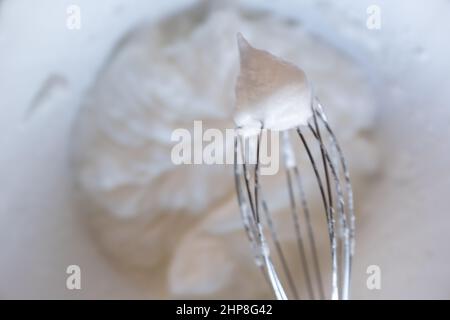 Whipped egg whites - beaten italian meringue on a whisk, closeup, copy space. Process of cooking meringue. Baking dessert concept. High quality photo Stock Photo