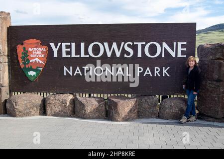 Female tourist standing next to the Yellowstone National Park sign on the north entrance, horizontal Stock Photo