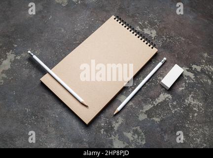 Photo of closed blank kraft sketchbook, pencils and eraser on concrete background. Stationery template. Stock Photo