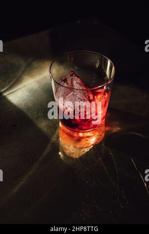 red hibiscus tea in glass with ice on brass reflective table in the sunlight Stock Photo