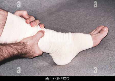 man with broken leg. male bandaging foot on the floor. The concept of a sore person with a limb injury. Close-up. Stock Photo