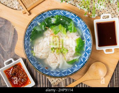 Fresh Meat Wonton soup with sauce and spoon in a plate isolated on wooden cutting board top view Stock Photo