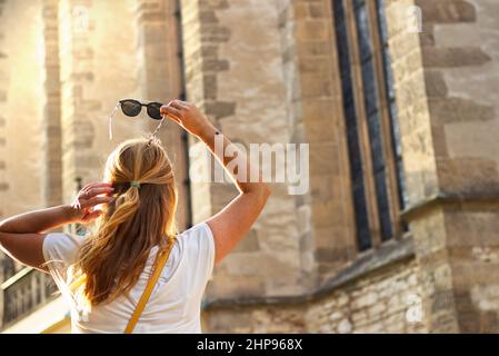 Blond hair woman with sunglasses in old town. Young woman holding sunglasses in hand and looking to church Stock Photo