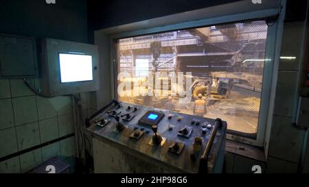 The central control room of the heavy industry plant. Fragment of operating room with monitors and the window with people working in the workshop. Stock Photo