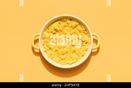 Above view with a portion of scrambled eggs in an enamel plate isolated on an orange background. Scrambled eggs plate minimalist on a colorful table. Stock Photo