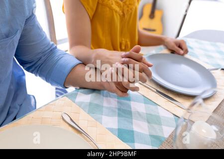 Midsection of multiracial couple holding hands while sitting at dining table Stock Photo