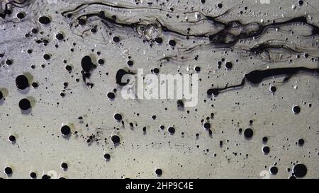 Top view of black ink drops flowing in liquid oil on metallic, grey background. Black balls of paint floating on the oily substance surface Stock Photo