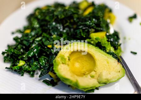 Macro closeup of kale green vegan salad on table with avocado half on white plate and fork as healthy meal showing texture and detail Stock Photo