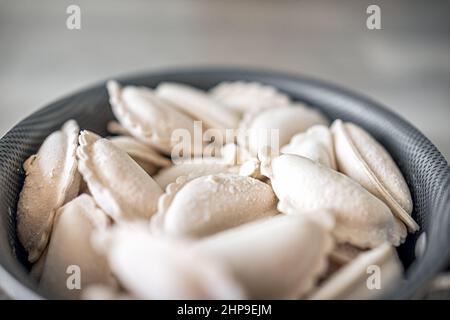 Cooking pot with frozen traditional Russian dumplings vareniki or Polish pierogi filled with potatoes or cheese for boiling closeup macro Stock Photo
