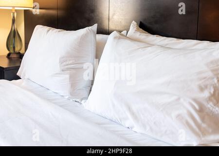 Bedroom room with lamp light and closeup of four clean white pillows with sheet on mattress bed headboard in modern hotel with nobody Stock Photo