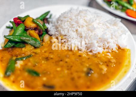 Macro closeup of orange curry healthy coconut squash dal Indian yellow split peas sauce food meal with white basmati rice on plate and vegetables as d Stock Photo