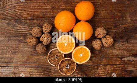 Oranges and walnuts on wooden background. Halves and dried oranges. Snack concept, mulled wine addition or autumn pie ingredients. Top view Stock Photo