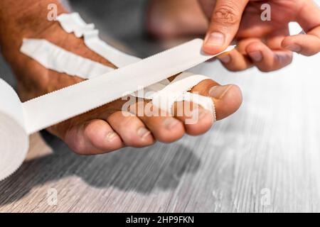 Closeup of young man body part leg feet on wooden floor taping fingers foot wrapped in athletic tape due to injury at jiu jitsu sport Stock Photo