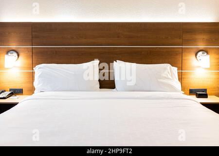 Bedroom empty room with illuminated lit lamp light and front view of white pillows with sheets on mattress bed headboard in modern hotel with nobody Stock Photo
