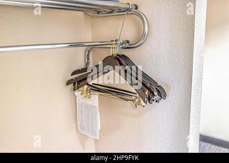 Closeup of closet hangers in empty room on pole stand in modern hotel or house room with note paper for dry cleaning Stock Photo
