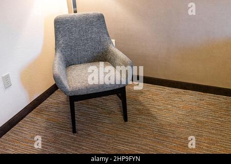 Closeup of one upholstered armchair chair with armrests by wall at with lamp light in home house interior room or hotel and carpet floor Stock Photo