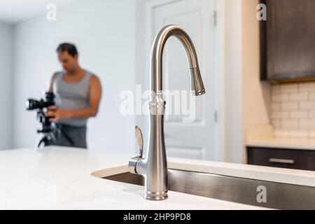 Kitchen room quartz countertop island in modern apartment home house with chrome faucet sink tap and man photographer in background for interior desig Stock Photo