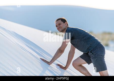 Happy young man smiling climbing on all fours on sand hill in white sands dunes national monument in New Mexico at soft sunset Stock Photo
