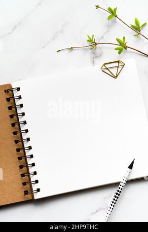 Mockup with blank album, notebook with spiral binder. Fresh spring leaves on off white marble stone background. Copy-space, place for your lettering Stock Photo
