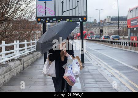 LONDON, FEBRUARY 19 2022, Pedestrian walks across Waterloo Bridge with an Umbrella as rainy weather continues as the aftermath of Storm Eunice. The Met Office issued two rare red warnings as the UK was hit by rain, snow and record-breaking 122 mph winds during the worst storm for 30 years. Stock Photo