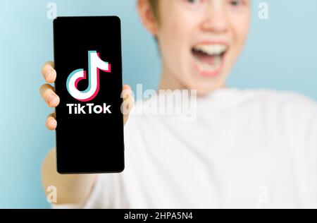 February 2022 - Tallinn, Estonia. Unfocused happy smiling boy with smartphone showing Toktok app logo Stock Photo