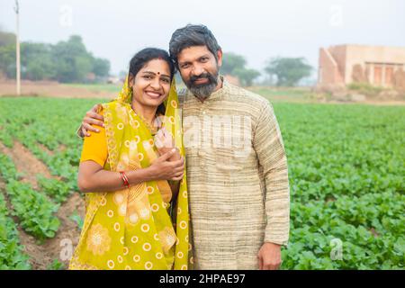 Portrait of happy indian rural farmer couple standing at agricultural field, Smiling traditional man wearing kurta and woman wearing sari looking at c Stock Photo