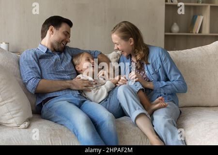 Happy young parents cuddling, tickling excited joyful cute daughter kid Stock Photo