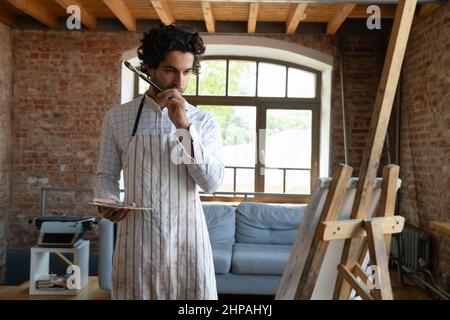 Pensive focused millennial artist creating new artwork. Stock Photo