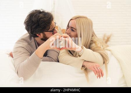 cute young European married couple laying on bed and forming heart shape with their hands, concept of love. High quality photo Stock Photo