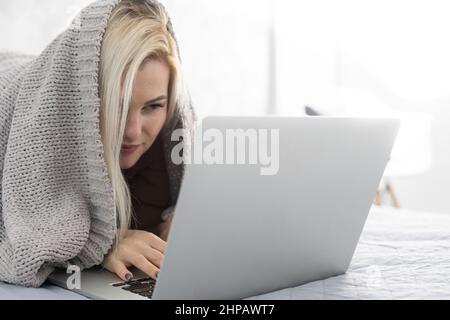 woman using laptop covered with blanket at the bedroom Stock Photo
