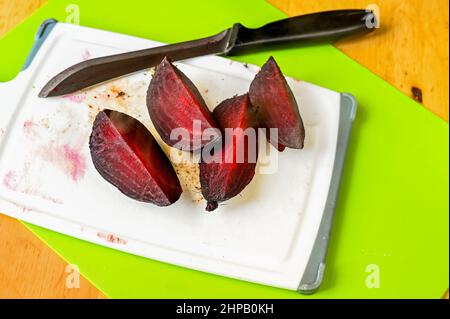 Sliced freshly baked hot beetroot on kitchen board with knife on table. Preparation salad. Stock Photo
