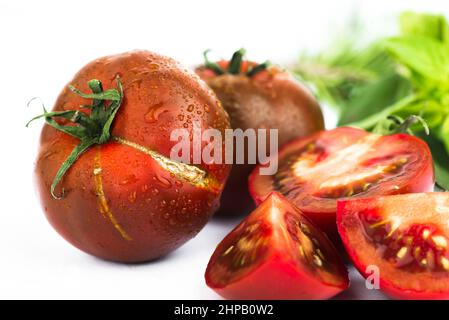 Dark red tomato (kumato), whole and halved, green leaf. Isolated on white background. Stock Photo
