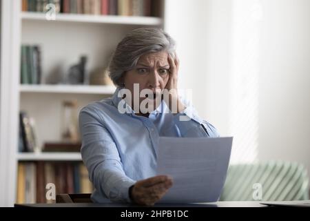 Shocked stressed middle aged woman looking at paper document. Stock Photo