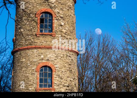 windows in an old round brick tower in front of full moon in blue sky Stock Photo