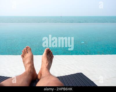 Close-up of the man's foot while resting on a sunbed in the blue water on the tropical pool and sea view. Holiday, vacation summer background with cop Stock Photo