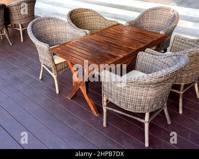 Empty rattan furniture, outdoor garden weave table set with wooden table and five chairs on the floor in the terrace near the steps in breakfast area Stock Photo