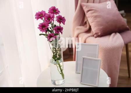 Vase with flowers and blank photo frames on table Stock Photo