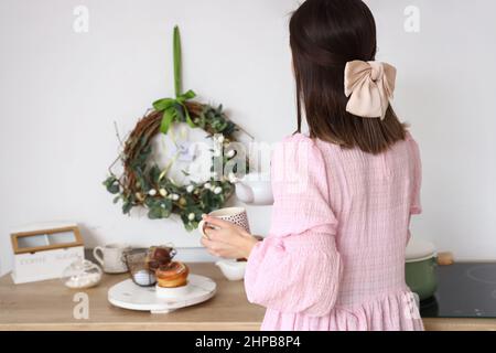 Woman pouring tea into cup near white wall with Easter wreath Stock Photo