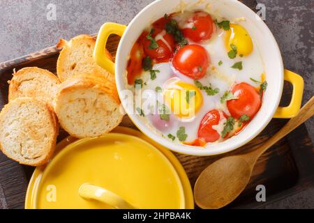 Portioned baked eggs in ceramic cocotte on white wooden table, breakfast closeup in the wooden tray on the table. Horizontal top view from above Stock Photo