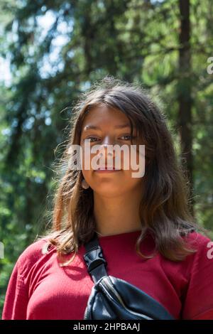 Portrait of a cute European teenage girl in the forest in summer on a sunny day, a girl in a burgundy dress, outdoor Caucasian teenage girl with sunli Stock Photo