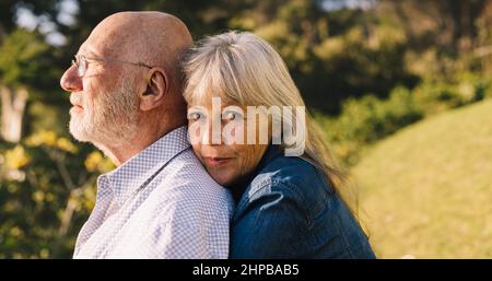 Beautiful elderly couple embracing each other in a park. Romantic senior woman looking at the camera while standing behind her husband. Mature couple Stock Photo