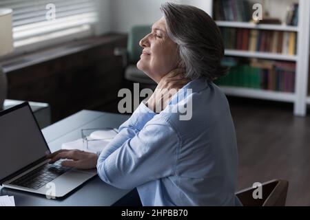 Stressed mature businesswoman suffering from stiff neck. Stock Photo