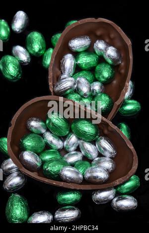 Colourful foil wrapped chocolate easter eggs in silver, and green with two halves of a large brown milk chocolate egg in the middle and mini eggs. Stock Photo