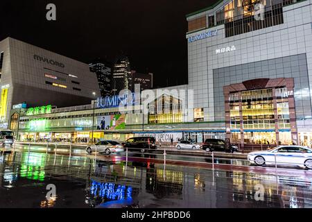 Shinjuku, Japan - April 1, 2019: Large shopping center exterior by station in downtown city with neon bright lights signs at night during rain with re Stock Photo