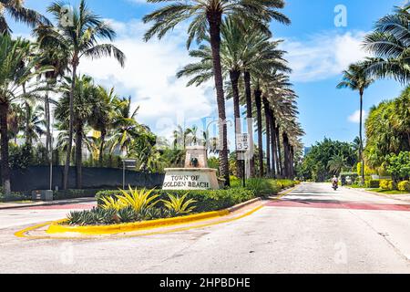 Miami, USA - July 18, 2021: Sign for welcome to Golden Beach in Miami, Florida with palm trees lining street road Collins Avenue on sunny day and blue Stock Photo