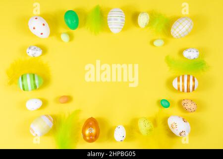 Easter frame with eggs and feathers on a yellow background. Minimal concept. View from above. Card with copy space for text. Stock Photo